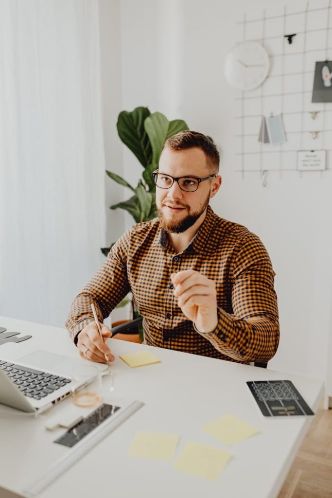 Man in checkered shirt working at desk with laptop in modern office setting.