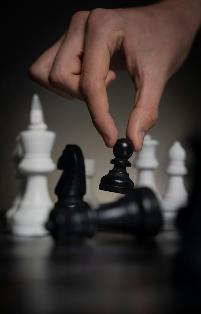 hand-moving-a-black-pawn-over-fallen-chess-pieces-batvi6gmewe