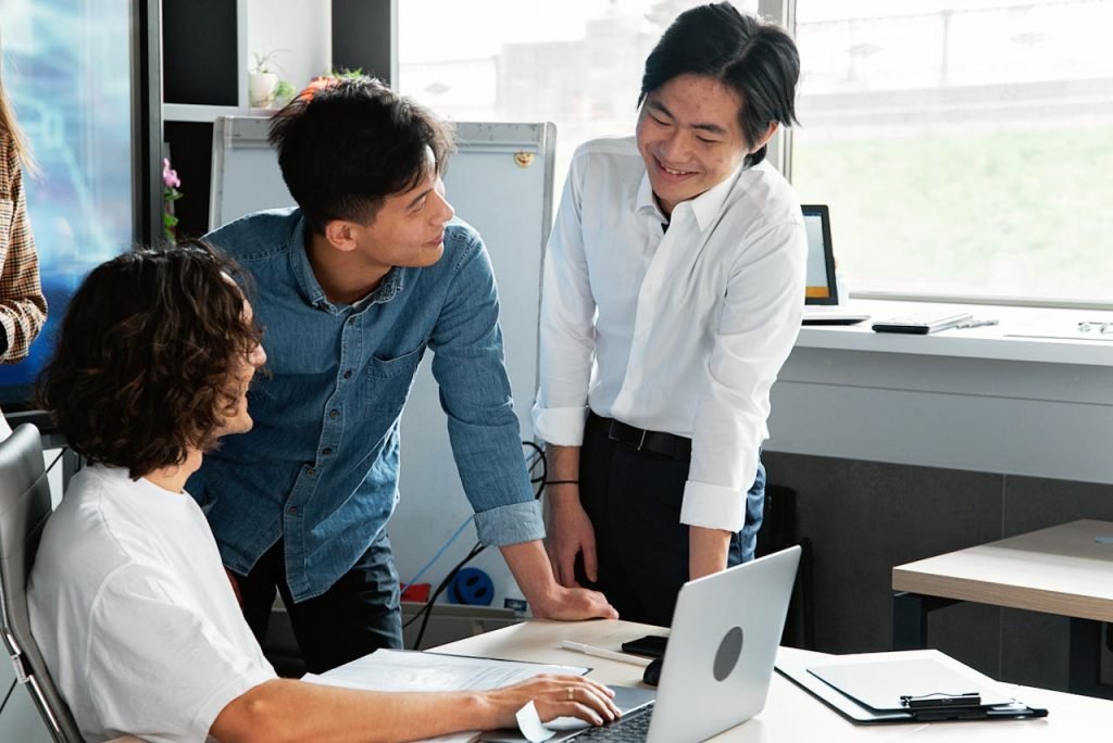 Colleagues engage in a brainstorming session around a laptop in a bright, modern office setting.